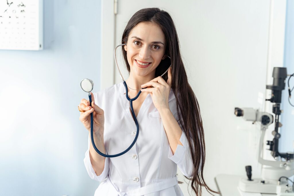 pexels photo 6749770 6749770 Confident female doctor holding a stethoscope while smiling in a clinic setting.